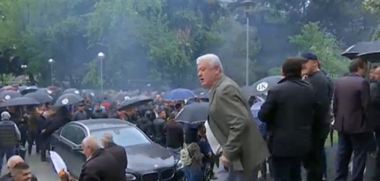 Protestuesit e PD-së sfidojnë shiun me çadrat “IK”, nis hedhja e kapsollëve dhe tymueseve [FOTO]